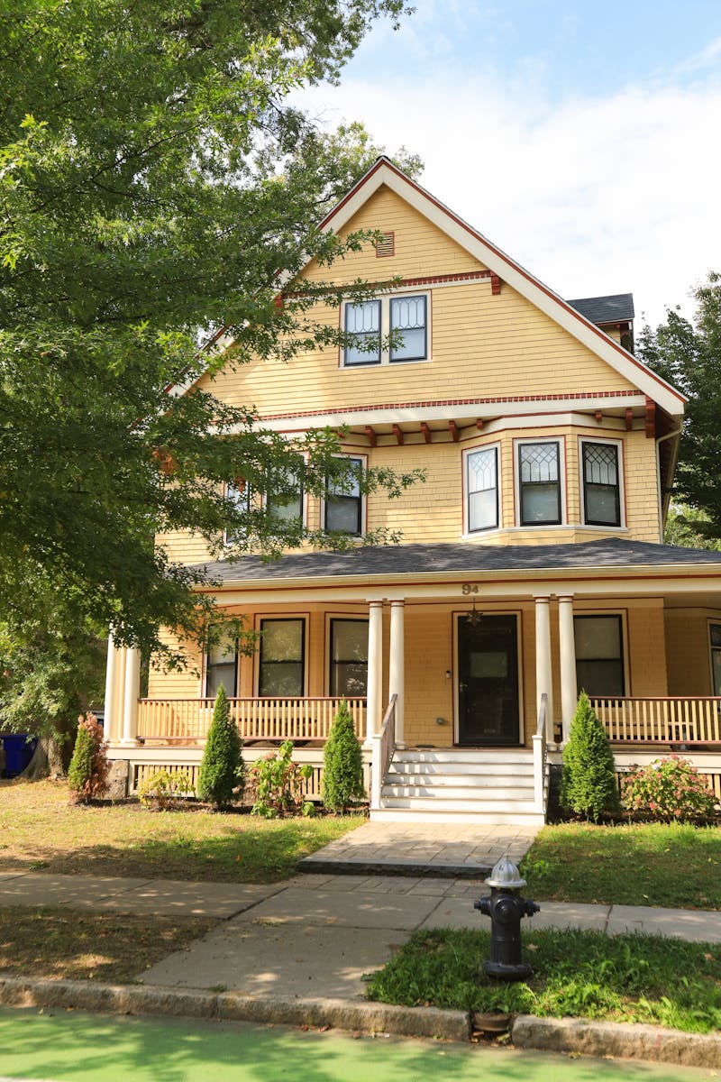 A beautiful yellow Victorian-style house with lush greenery and a welcoming porch.